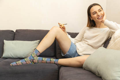 Woman sitting on a couch wearing colorful socks and denim shorts, smiling. Seasons of Life Socks by Roberta Pacino